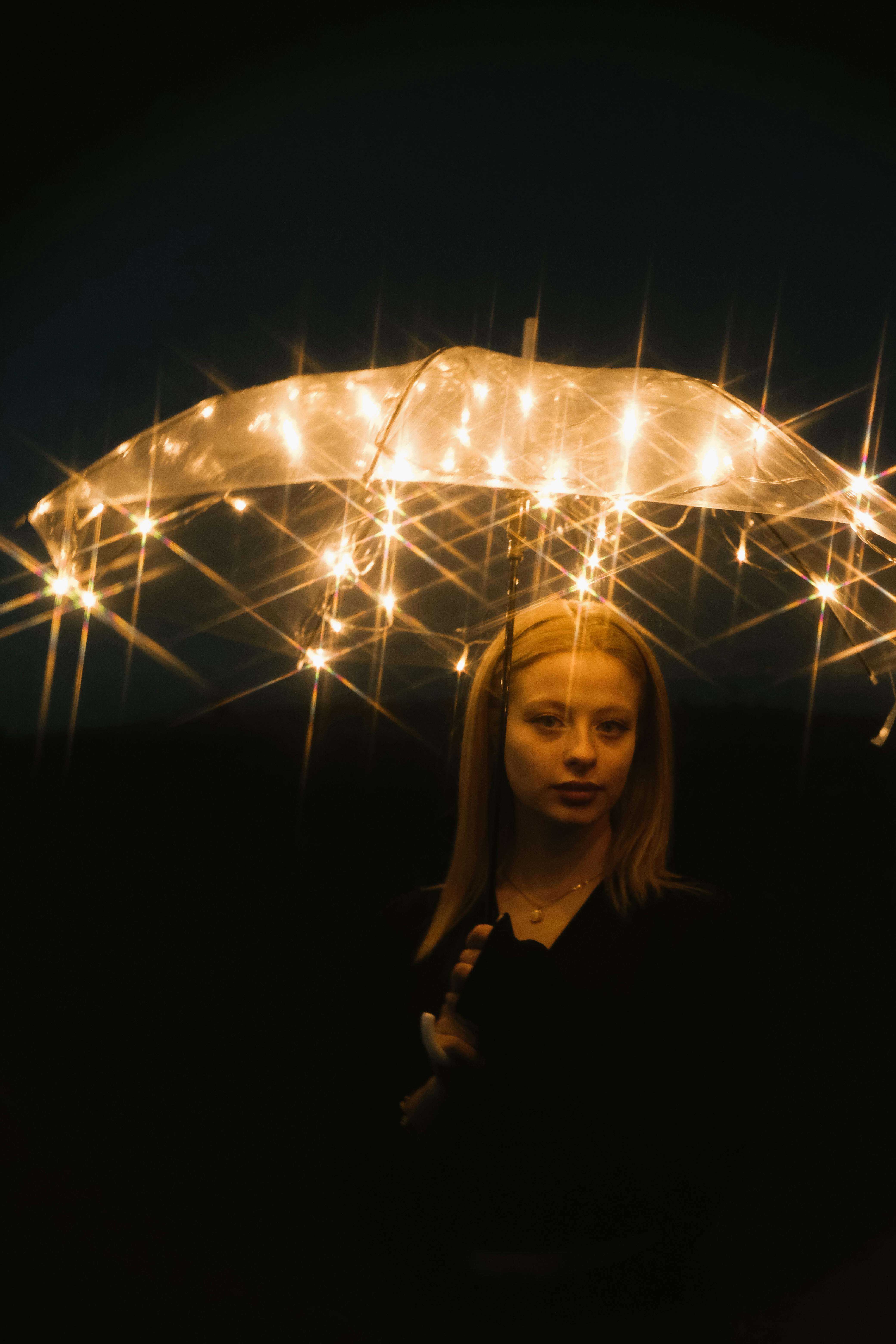Artistic portrait of a woman holding a glowing umbrella under starry lights at night.