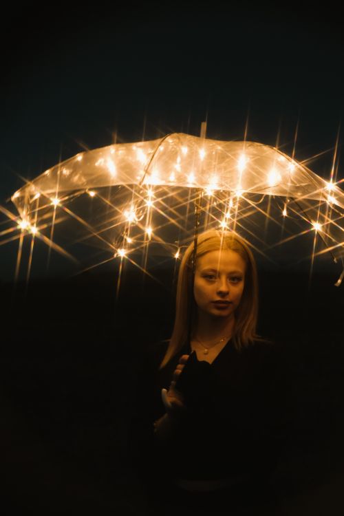 Free Artistic portrait of a woman holding a glowing umbrella under starry lights at night. Stock Photo