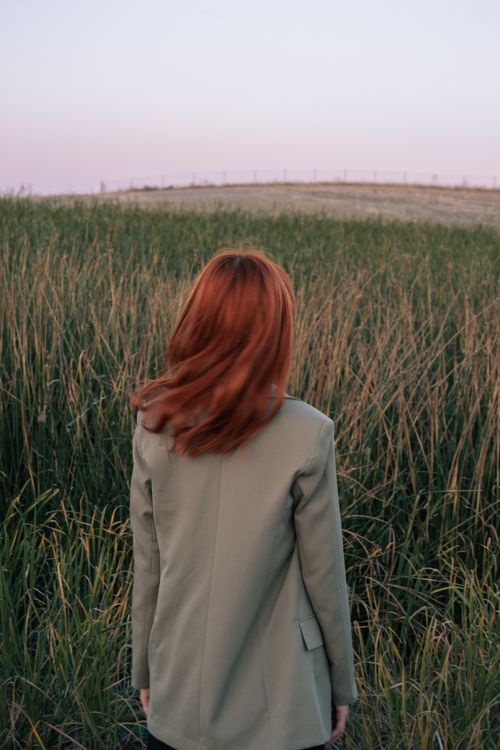 Free Red-haired woman standing in a field at sunrise, capturing a serene rural landscape. Stock Photo