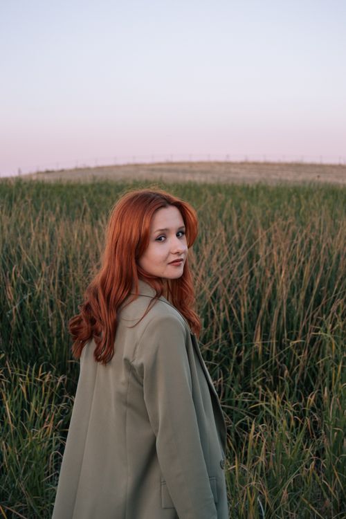 Free Beautiful redhead woman standing in a green meadow at sunset, showcasing natural beauty fashion. Stock Photo