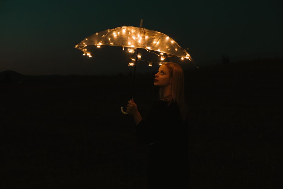 Woman gazing upward holding a glowing umbrella against a mystical night sky