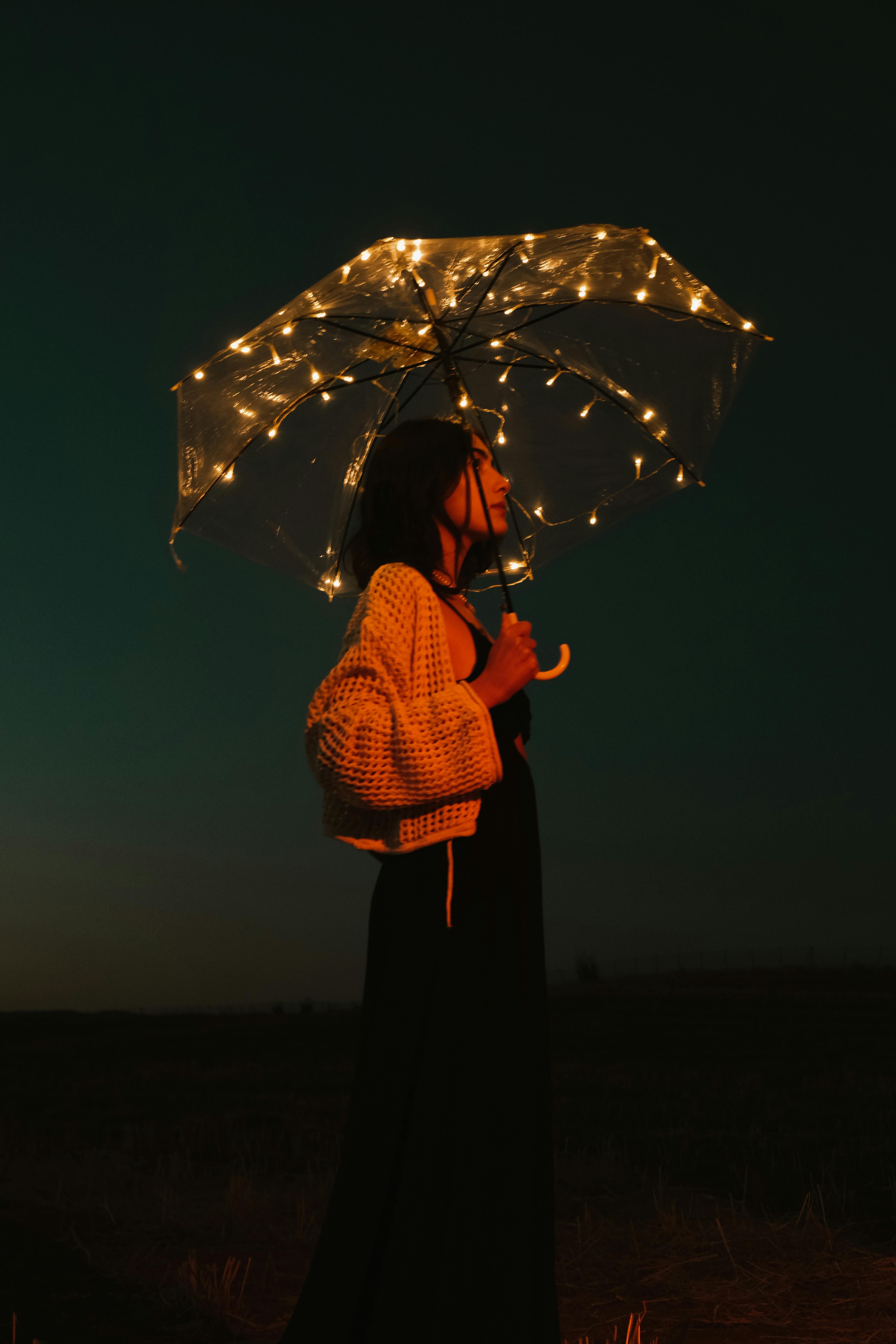 Woman holding illuminated umbrella against night sky, creating a magical silhouette.