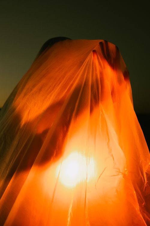 Free A haunting silhouette features under an illuminating orange light, draped in translucent material. Stock Photo