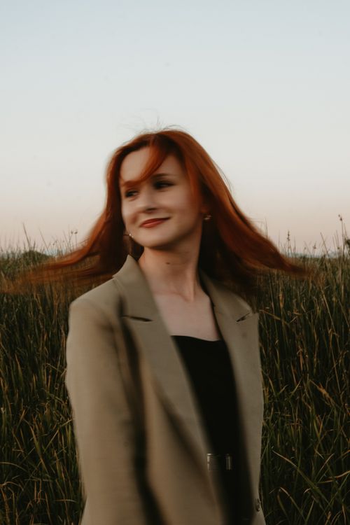Free A smiling redhead woman in a field, tossing her hair and showcasing fashion with elegance. Stock Photo