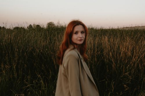 Free Elegant red-haired woman in stylish jacket strolling through countryside at sunset. Stock Photo
