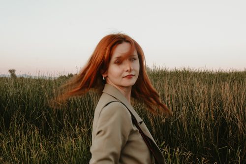 Free Stylish woman with red hair in a serene countryside field setting at twilight. Stock Photo