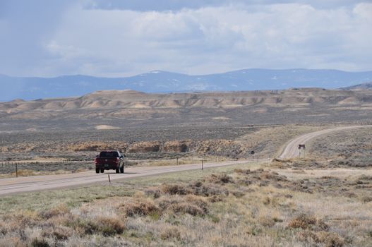A solitary truck travels along a desert highway with mountainous terrain in the distance.