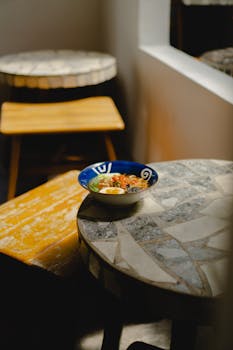 A bowl of Indonesian ramen on a mosaic table in a warm café interior.