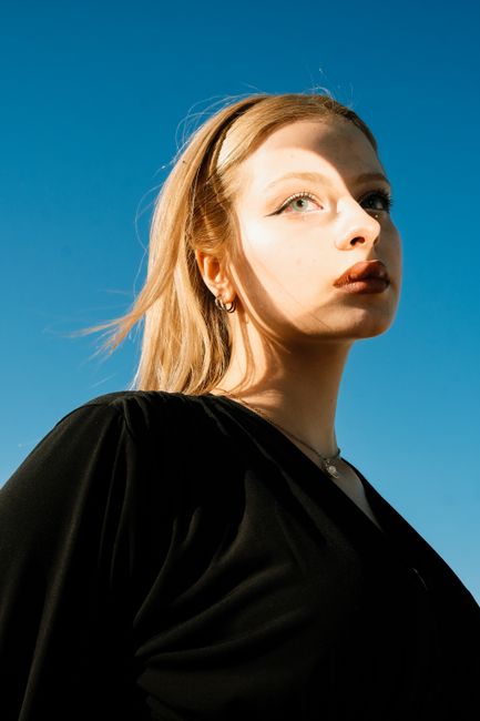 Portrait of a woman posing elegantly in a black blouse with a clear blue sky background.