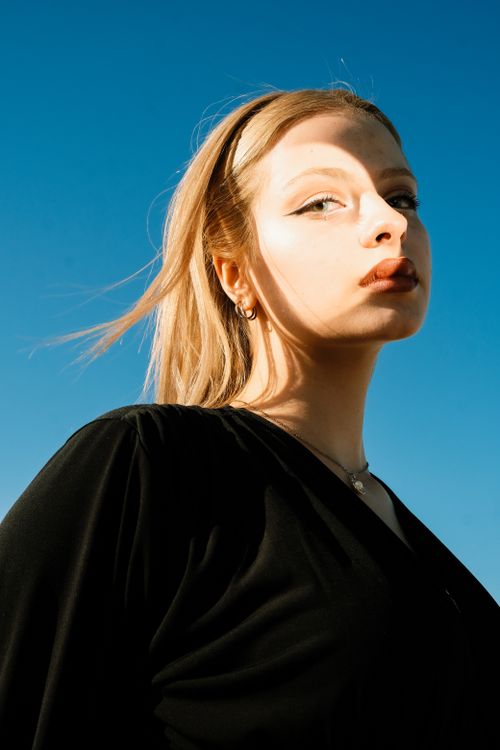 Free Striking portrait of a woman with sunlight casting soft shadows, wearing a black blouse. Stock Photo