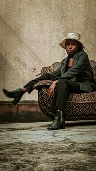 Portrait of a fashionable African woman sitting in an armchair, wearing a hat and stylish outfit in Lagos, Nigeria.