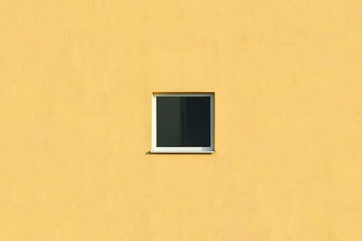 A small isolated window on a vibrant yellow wall offers minimalist architectural design.