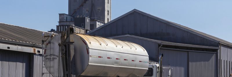 A large semi-trailer truck parked at an industrial grain warehouse under clear skies.