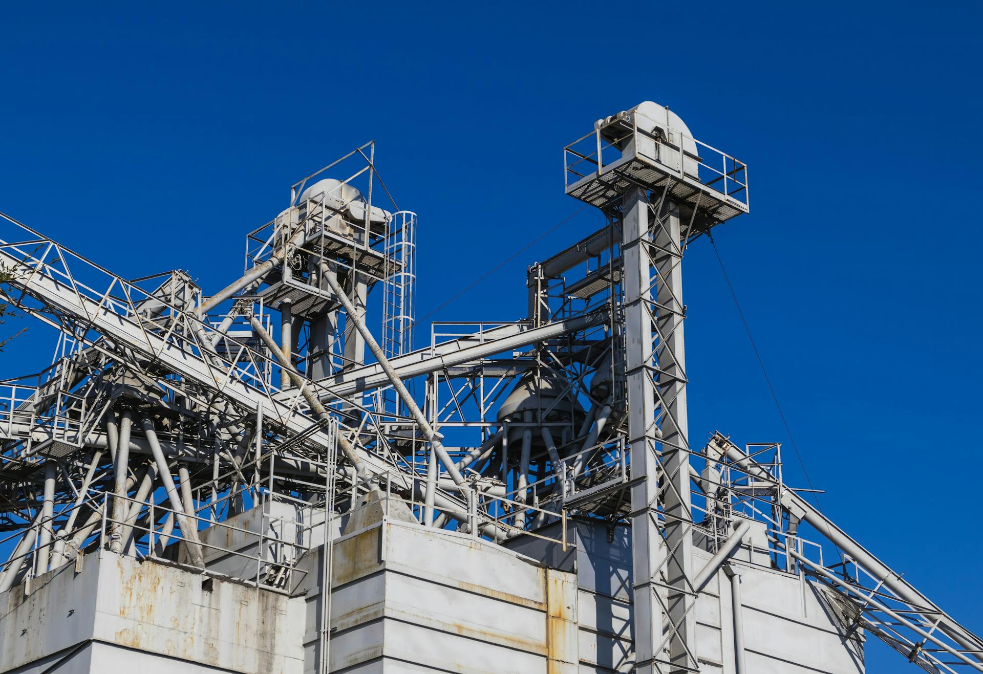 Detailed view of metal industrial structures with pipes and beams against a clear blue sky.