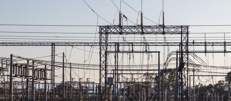 早朝の高圧変電所の鋼構造物と送電線。電気料金改定を伝える経済ニュースのイメージ。