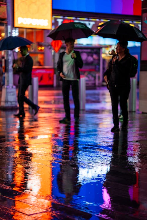 People with Umbrellas on the Rain-Drenched Pavement