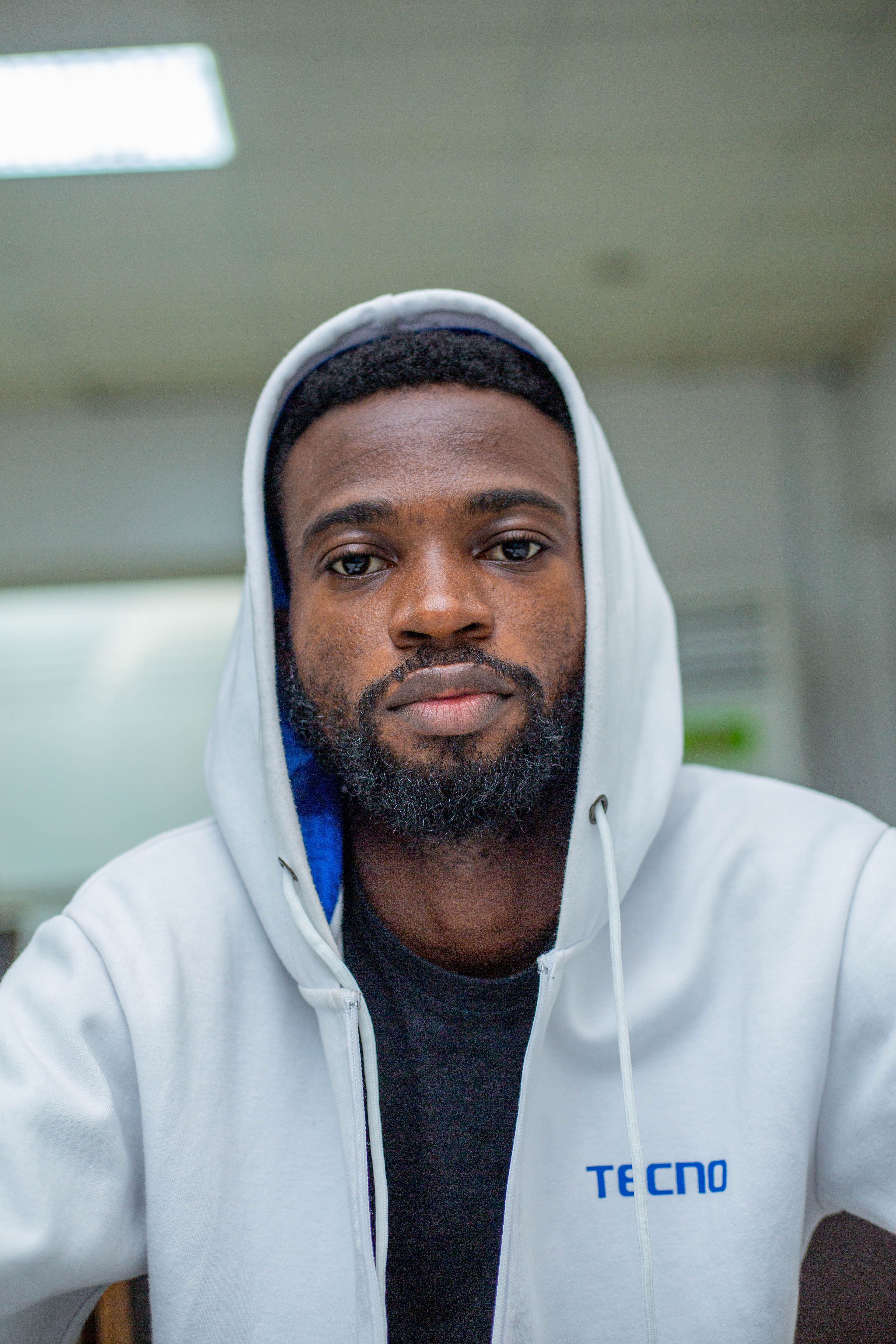Close-up portrait of a bearded man in a white hoodie with a serious expression, captured indoors.