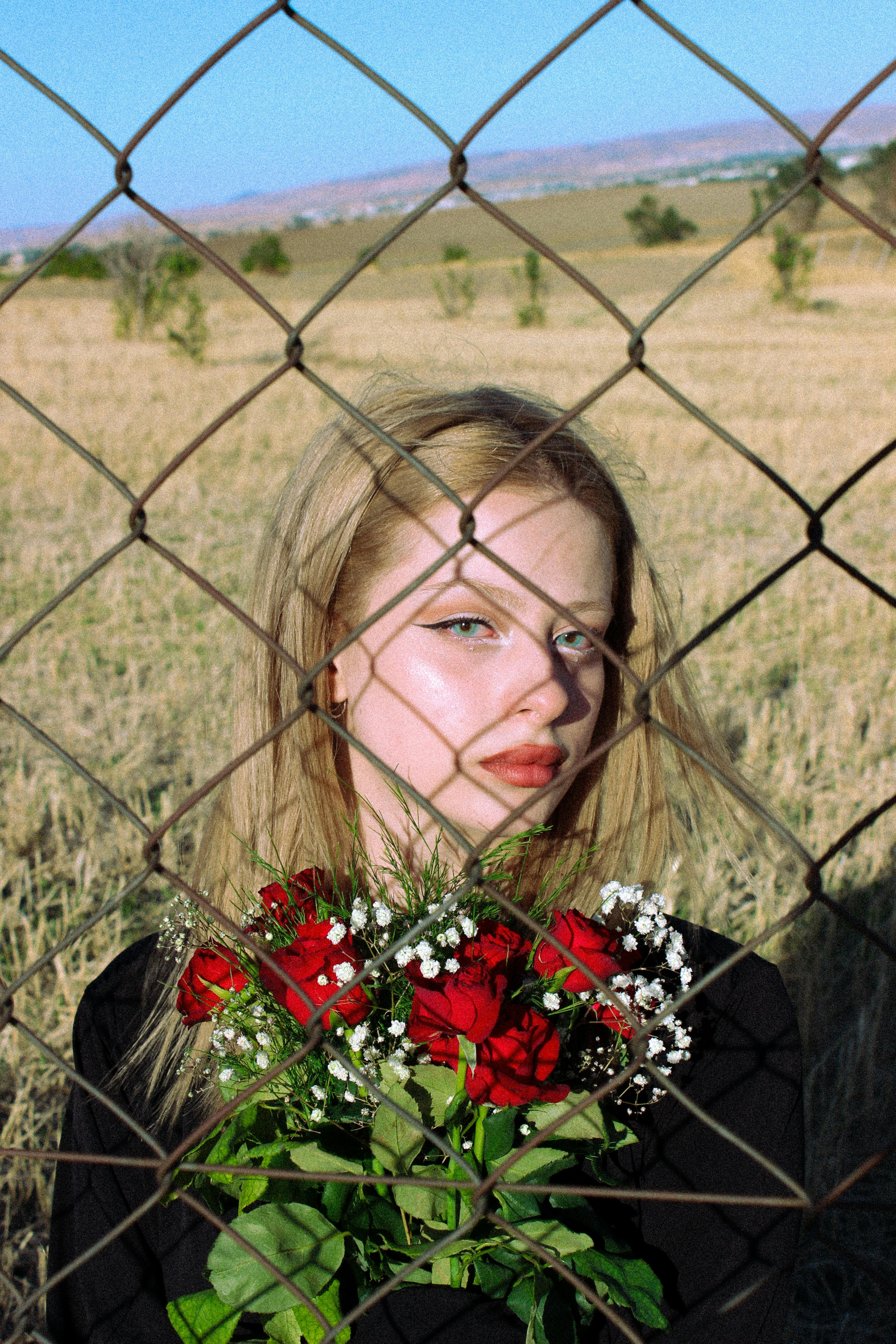 young woman with a bouquet of red roses behind a chain link fence