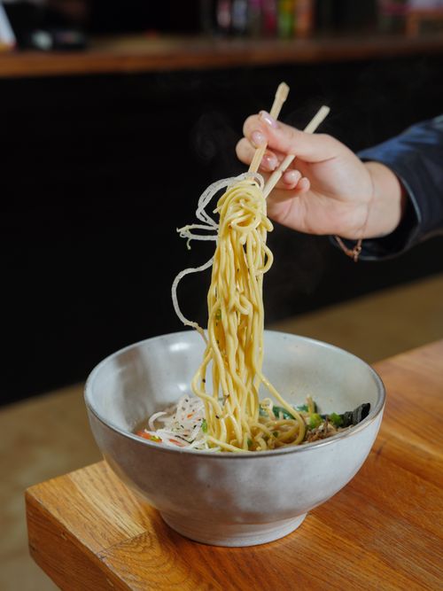 Free A close-up of a hand using chopsticks to lift noodles from a bowl, indoors. Stock Photo