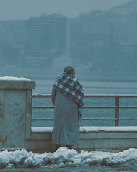 A person stands by a snowy riverside in Baku, Azerbaycan, wrapped in a warm coat.