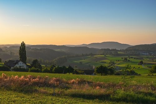 Free Serene rural landscape with rolling hills and fields under a warm sunset glow. Stock Photo