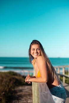 一位穿着泳衣的年轻女子靠在栏杆上，享受着阳光明媚的海滩