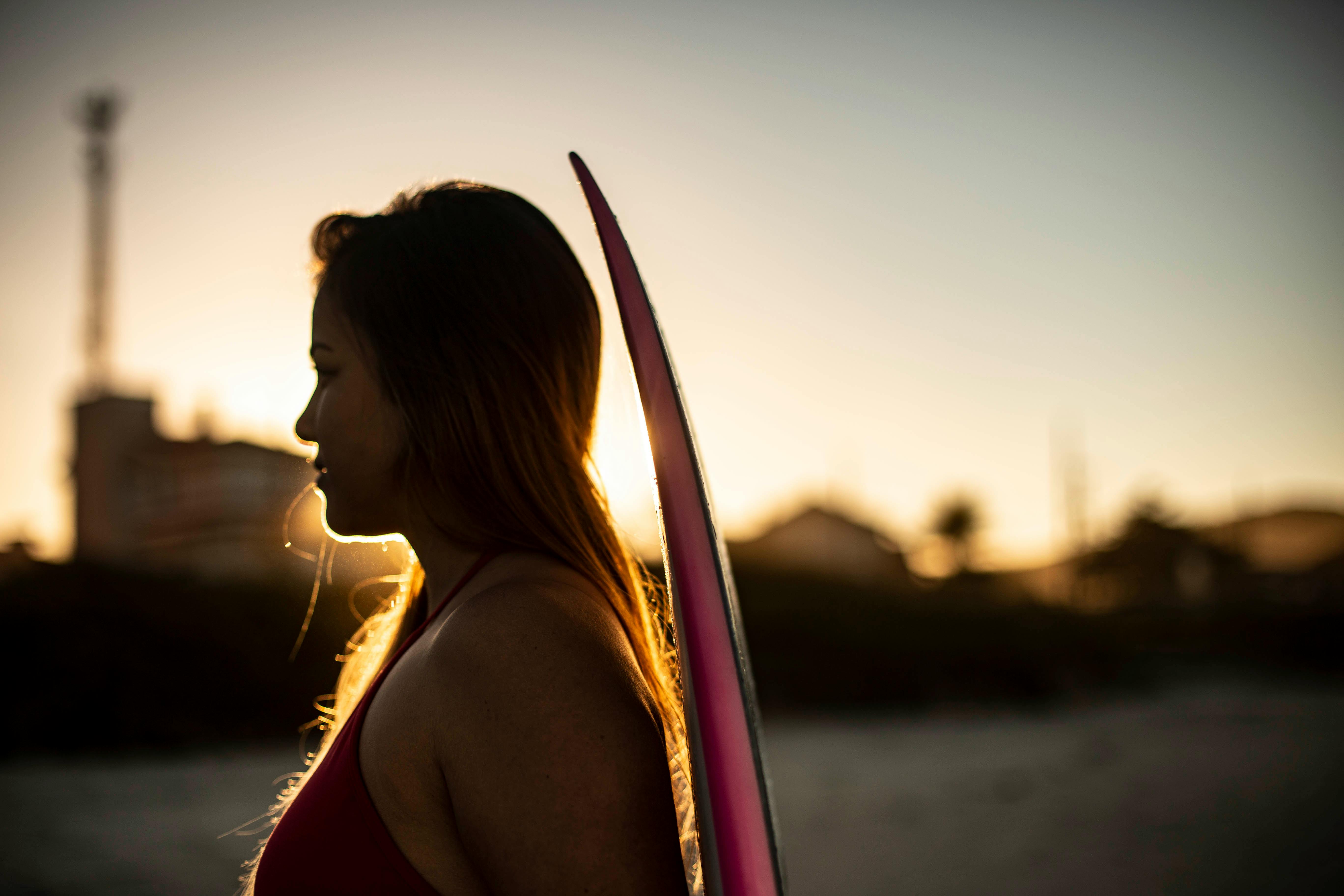 日落背景下，一个女人拿着冲浪板的剪影迷人而宁静，散发着冒险的气息
