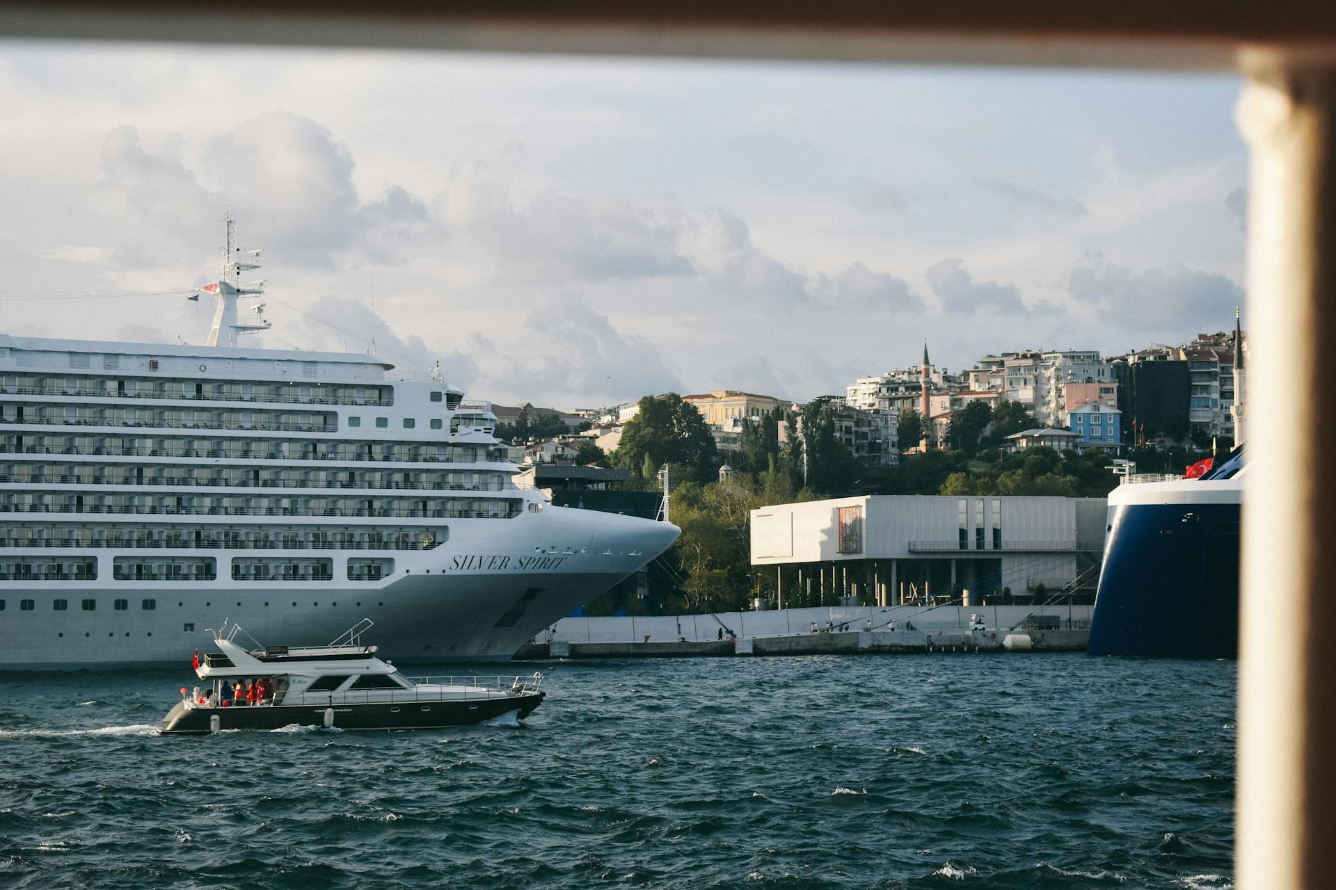 Capture of a luxury cruise ship and a motor yacht near urban buildings, set against a scenic seaside backdrop.