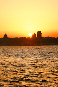 Silhouette of a city skyline at sunrise, casting vibrant colors over the ocean.