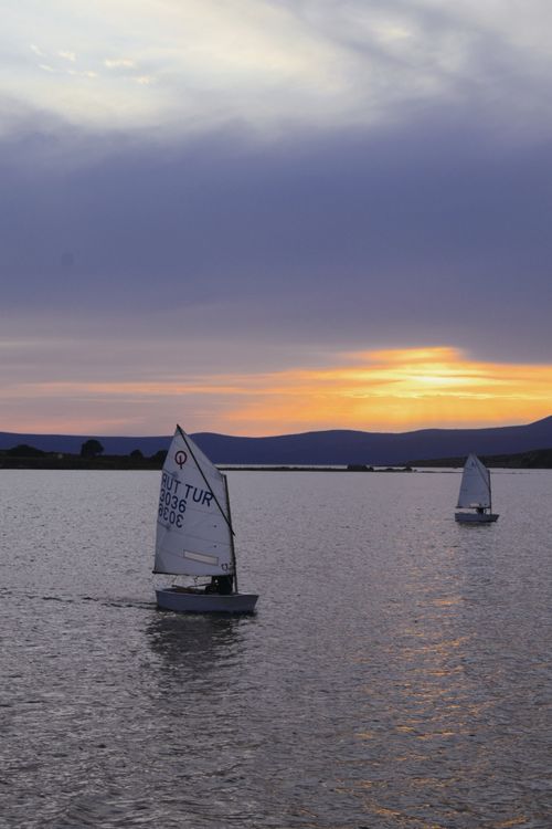 Free Two sailboats glide on a peaceful lake under a vivid sunset sky, capturing a serene moment in nature. Stock Photo
