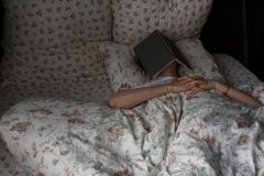 Woman relaxing in bed with book on face, floral bedding, creating a cozy vibe.