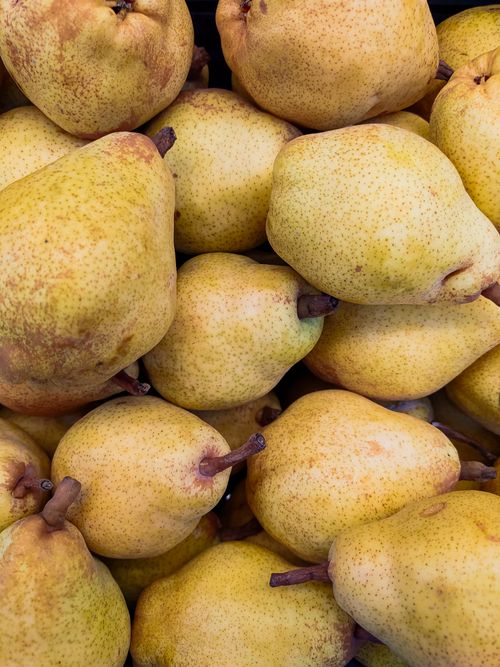Free Close-up of fresh yellow pears stacked at a market stall, showcasing their vibrant and juicy appearance. Stock Photo