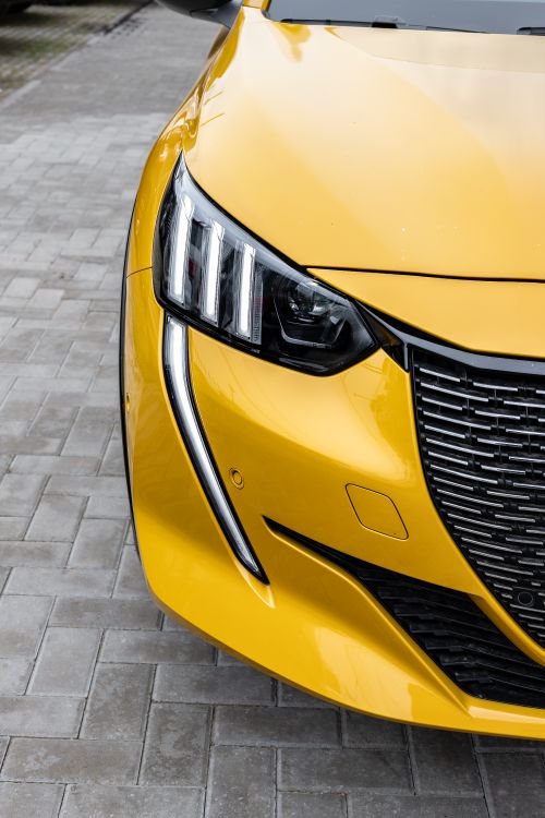 Free Elegant yellow car showcasing modern headlight design and grill on paved background. Stock Photo