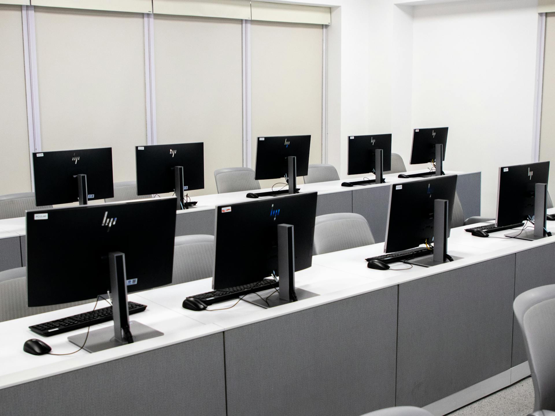 An empty computer lab with modern desktop setups and ergonomic chairs.