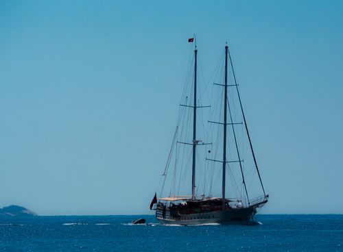Free A classic sailboat journeys across the calm blue sea under clear skies. Stock Photo