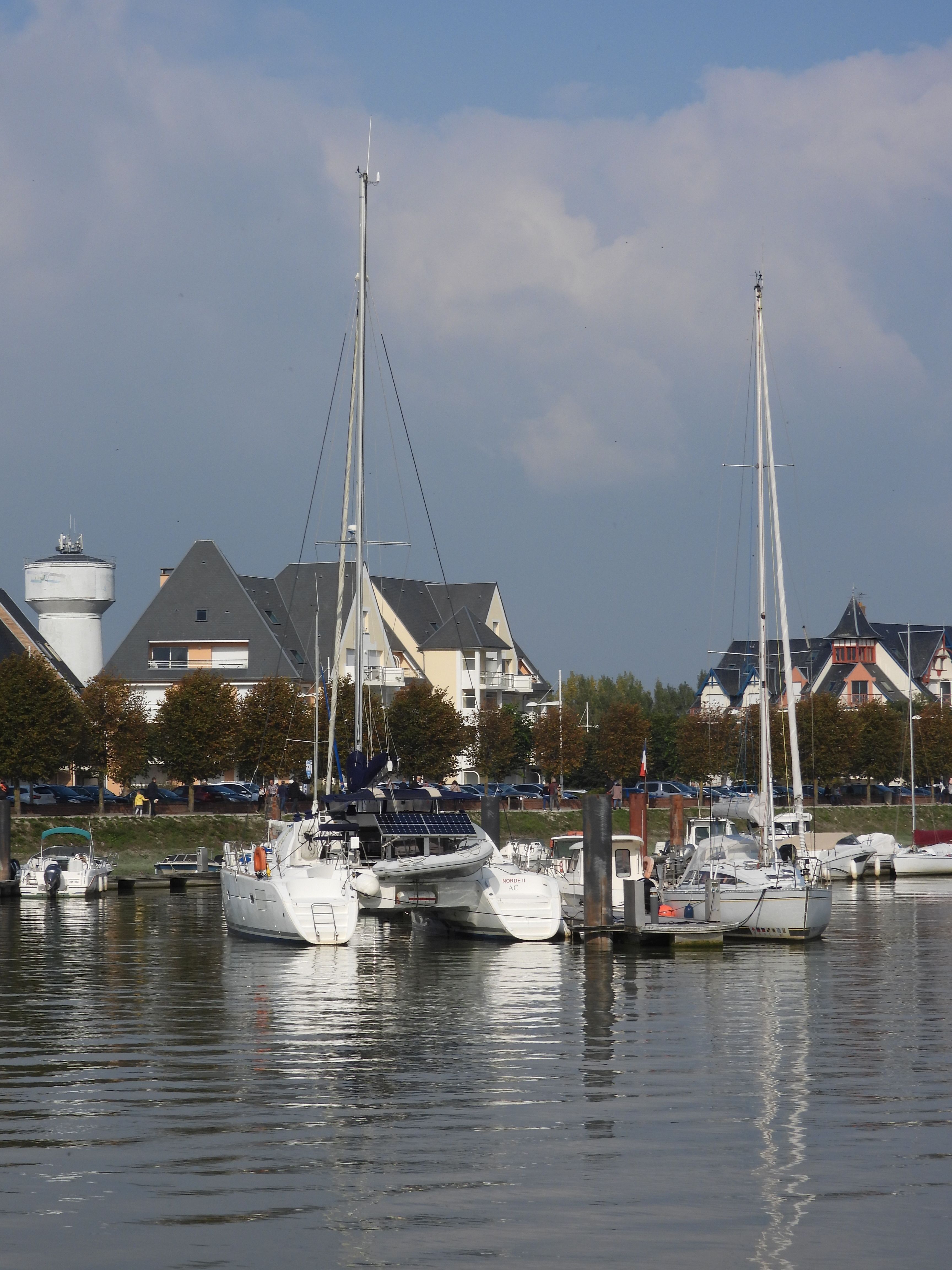 Sailboats docked at Le Crotoy marina with scenic village backdrop.