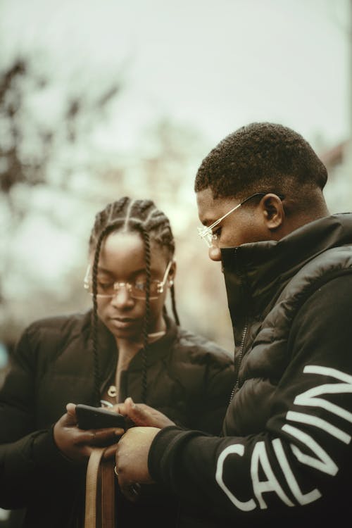 Young Man and Woman in Black Puffer Jackets Holding a Smart Phone