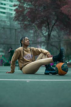 Teen girl in sportswear posing on outdoor basketball court, expressing style and youth.