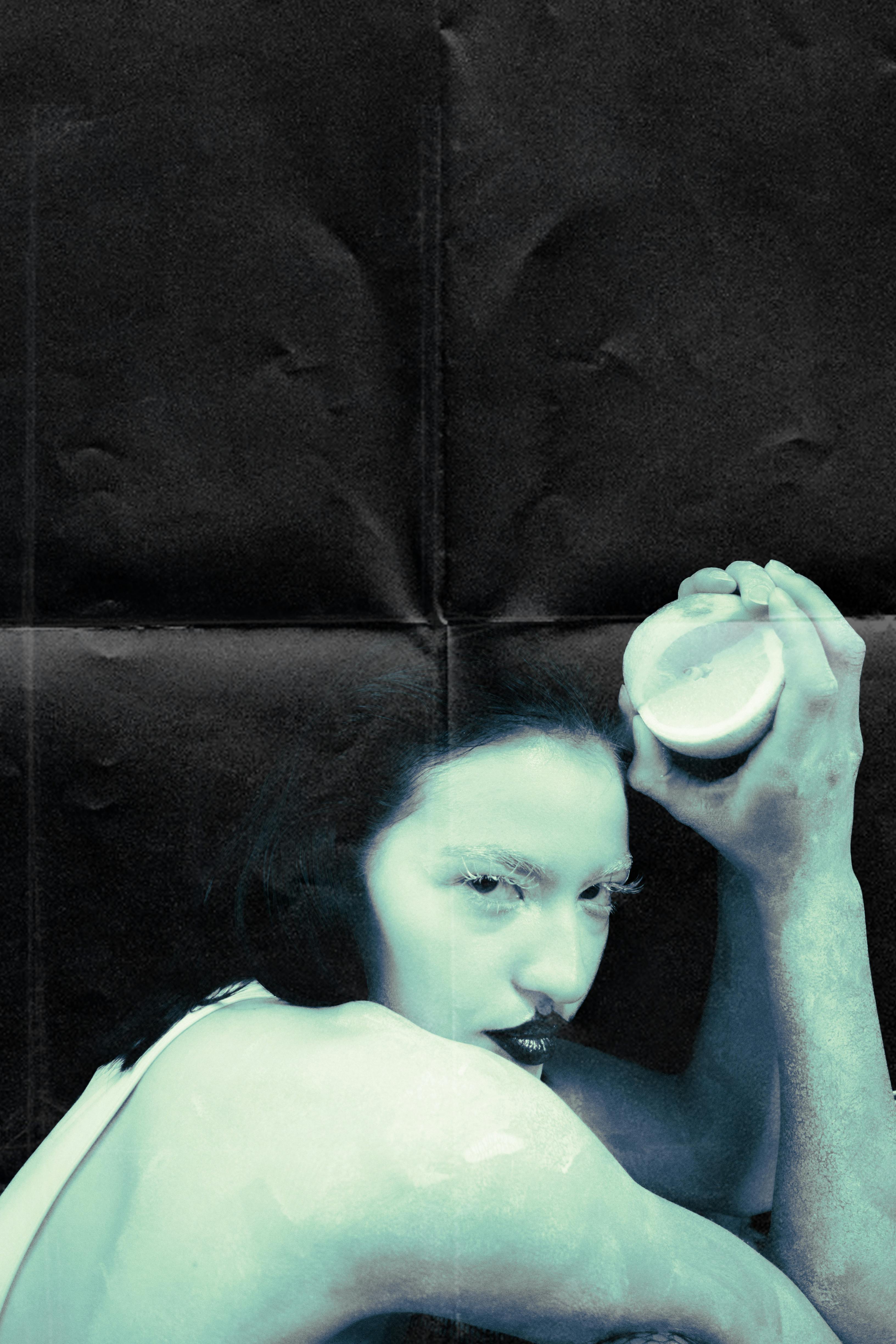 Surreal portrait of a woman holding a fruit against a black background.