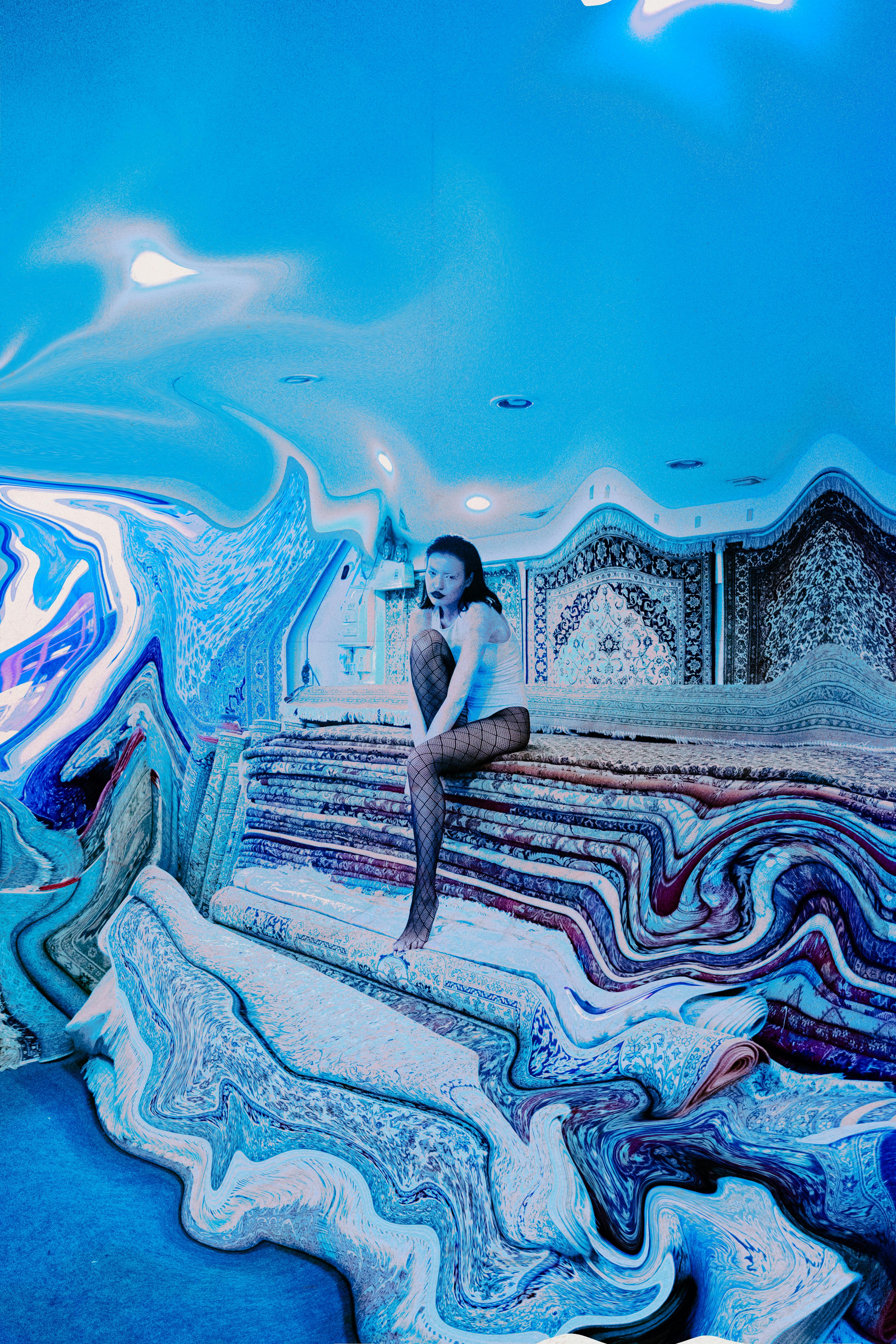 Artistic photo of a woman posing on distorted carpets with a surreal effect and blue lighting.