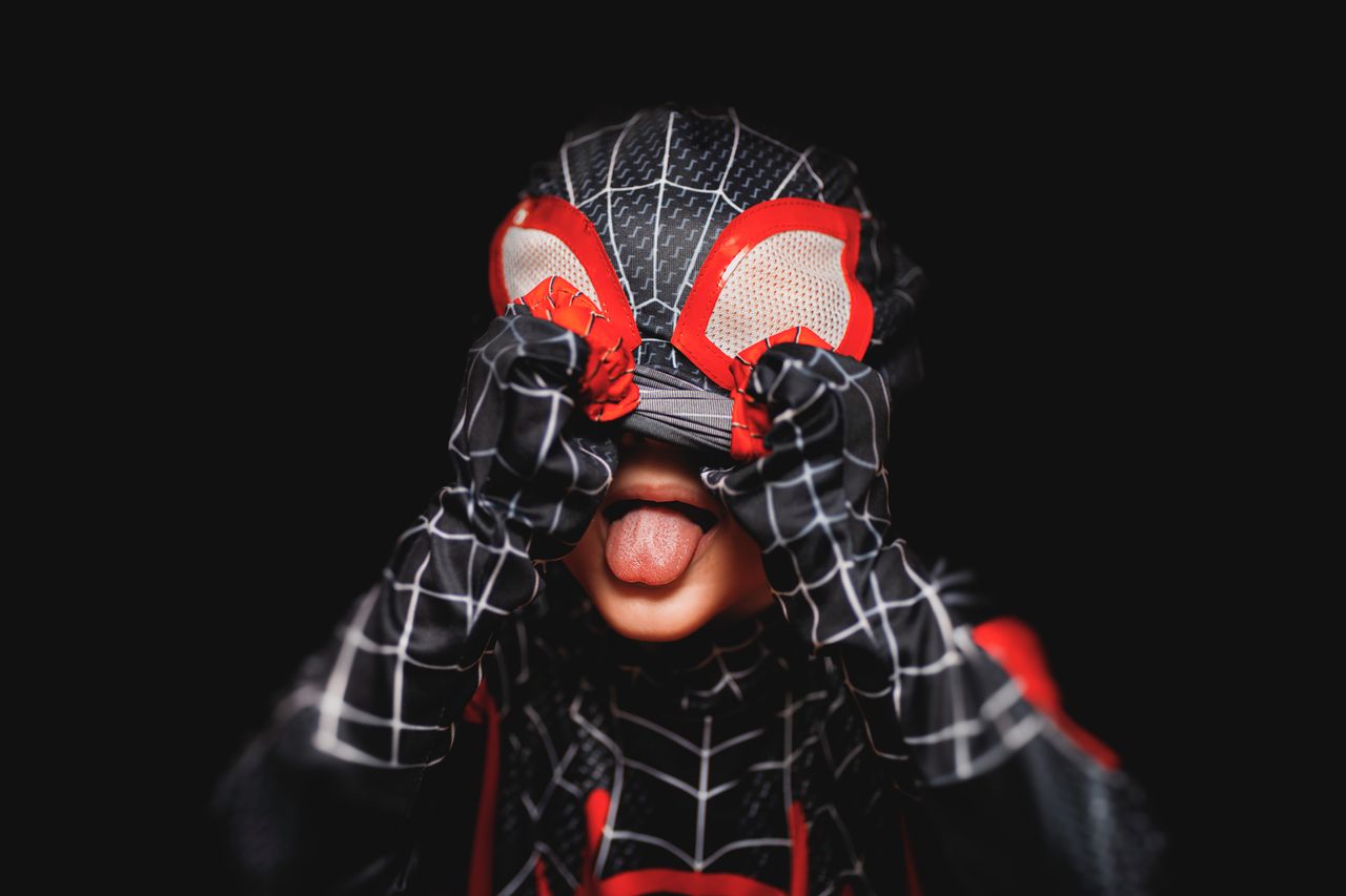 a playful child in a spider man costume playfully sticks out their ton