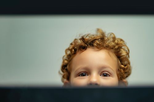 Free A young child with curly hair peeking playfully from below, creating a joyful and innocent mood. Stock Photo