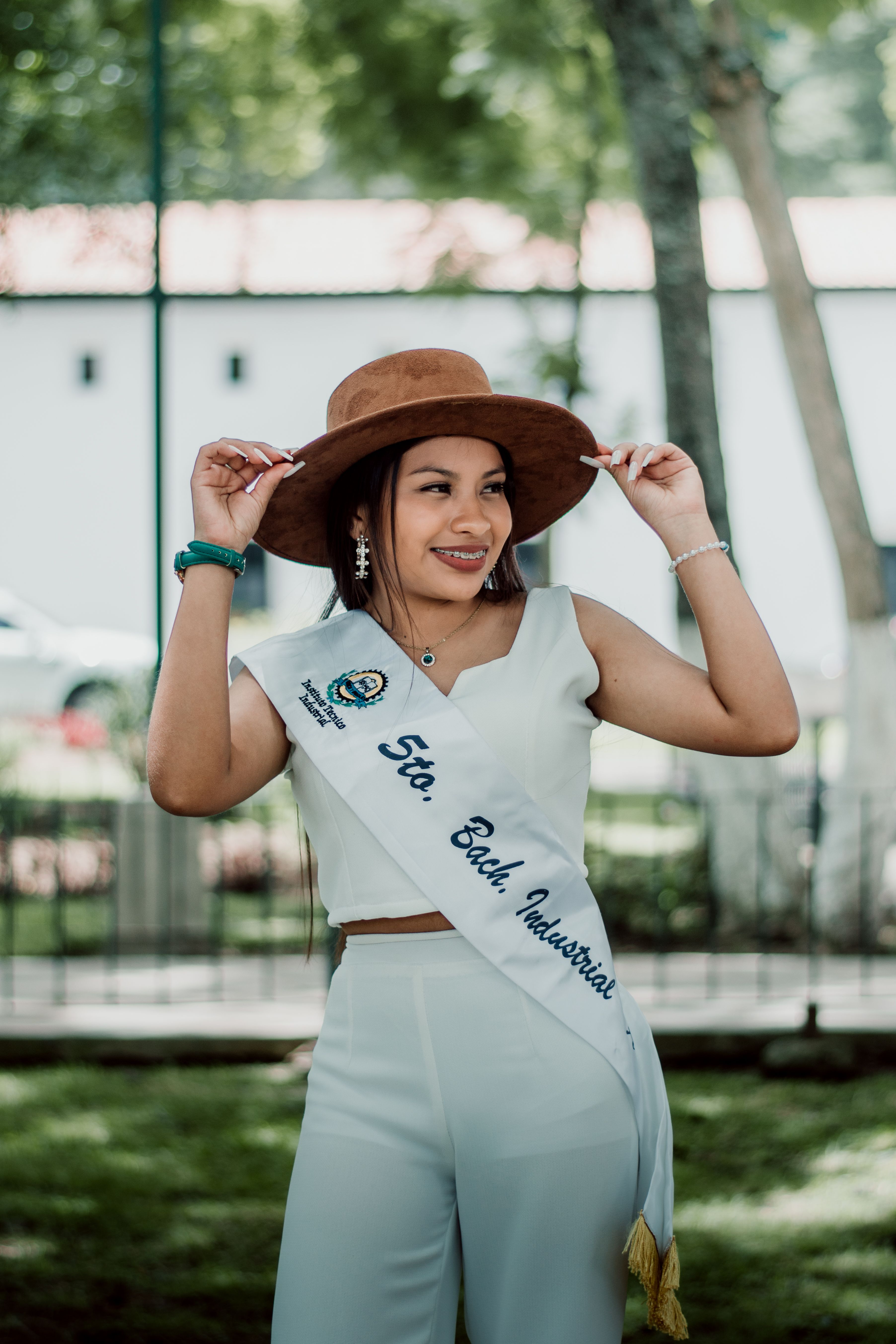 Smiling woman in white attire and brown hat with sash, posing outdoors in Antigua Guatemala.