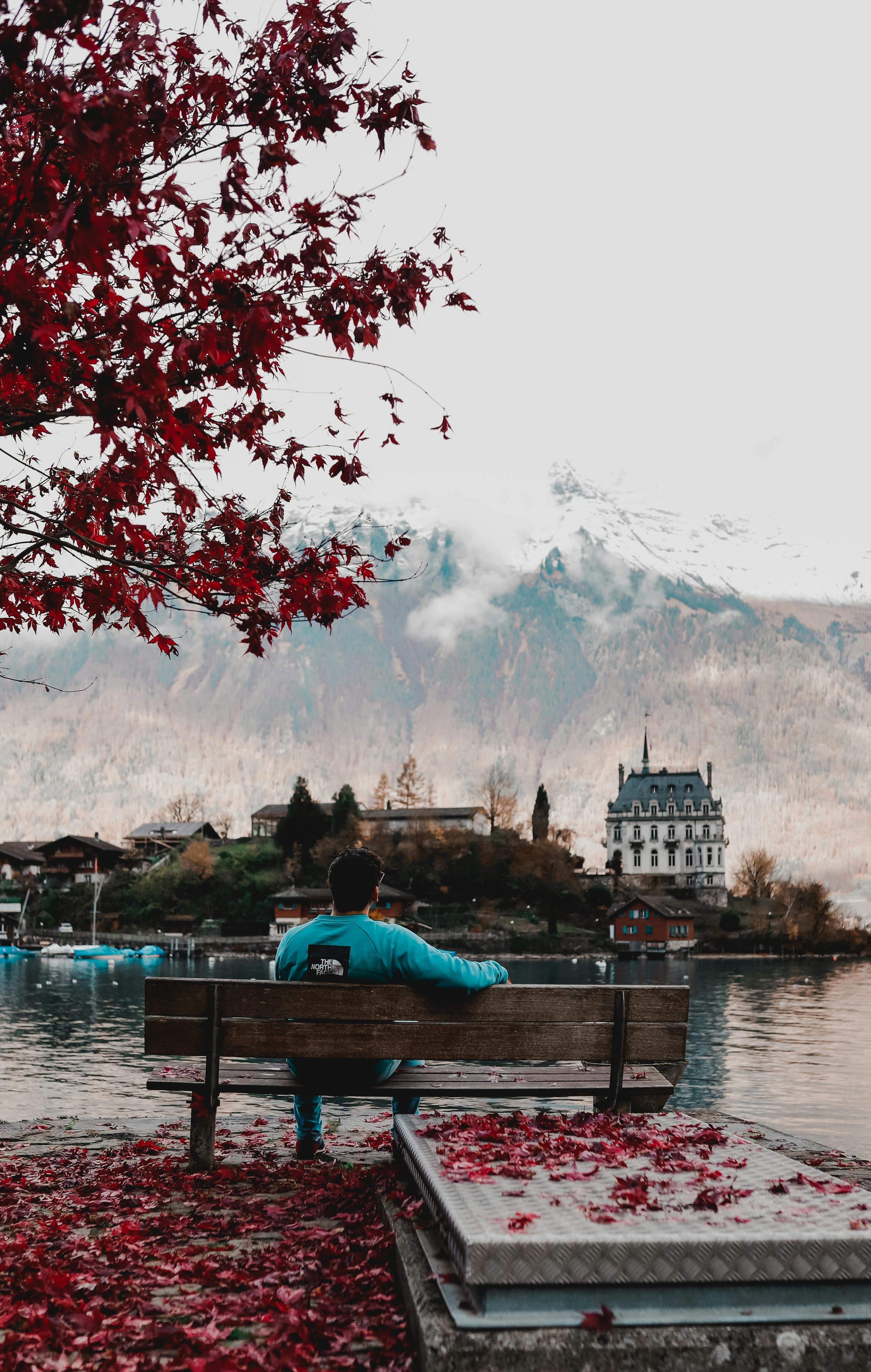Man sitting on a bench by Lake Brienz, Iseltwald, with autumn foliage and castle view.