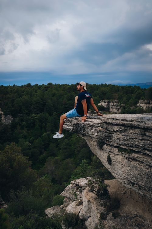Free A man sitting on a rocky cliff edge, enjoying a scenic forest view. Stock Photo
