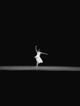 A graceful ballerina dances alone on stage in a monochrome setting, showcasing artistry and poise.