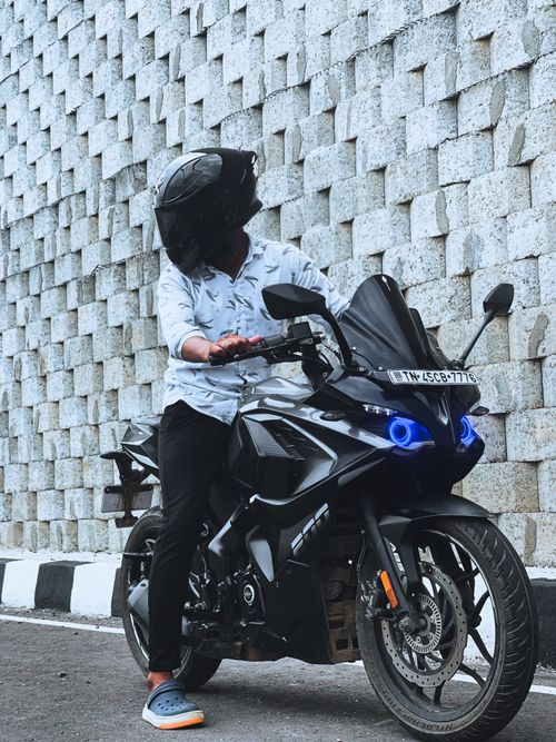 Free A man in a helmet sits on a sleek motorcycle against a textured urban wall, exuding modern style. Stock Photo