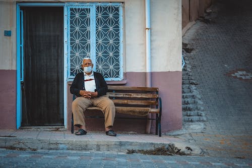 Elderly Man in a Face Mask Sitting on a Bench 