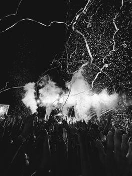 Exciting black and white concert scene with crowd, smoke, and confetti enhancing the atmosphere.
