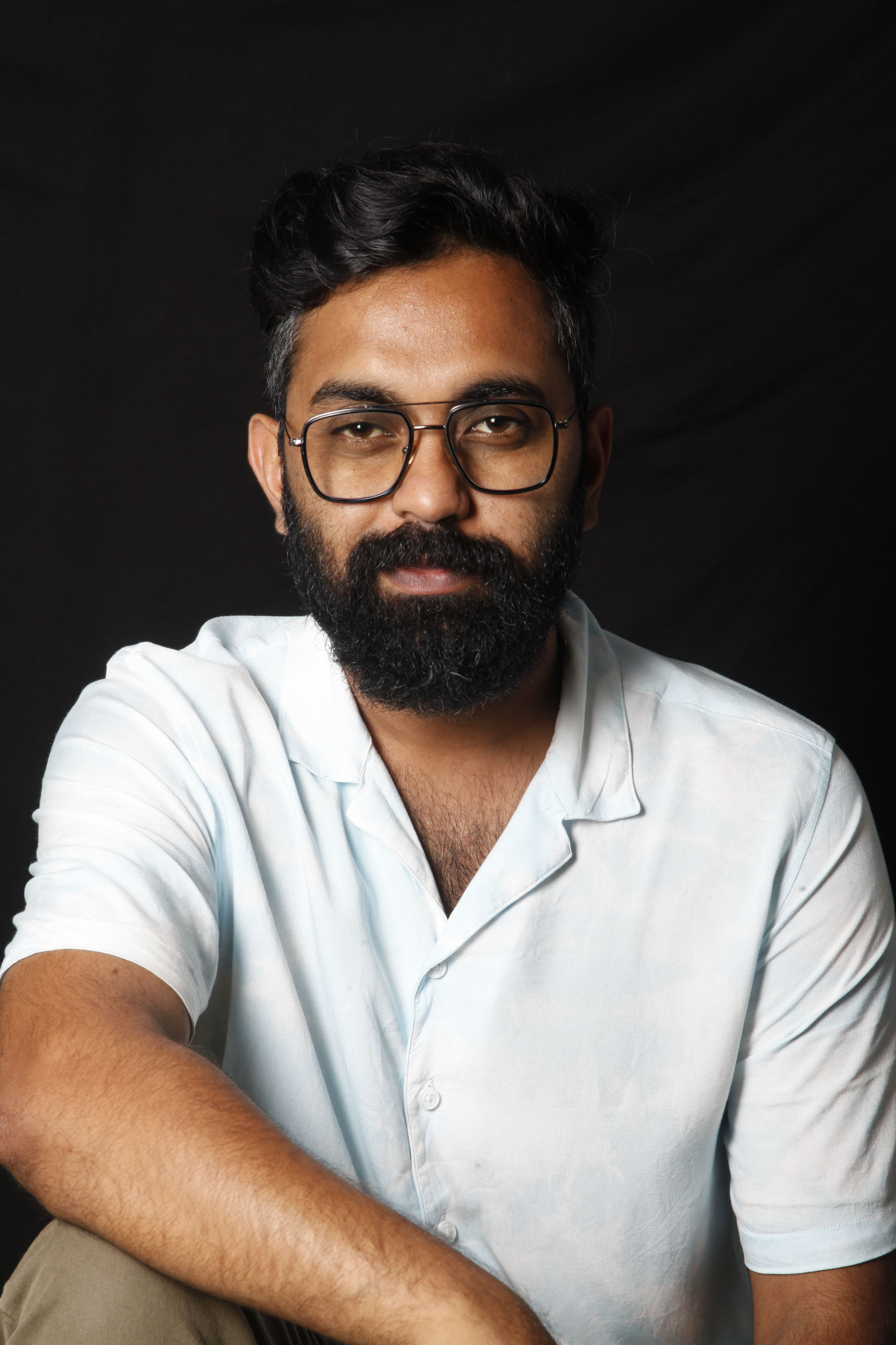 A bearded man with glasses wearing a white shirt, showing a calm expression against a dark background.